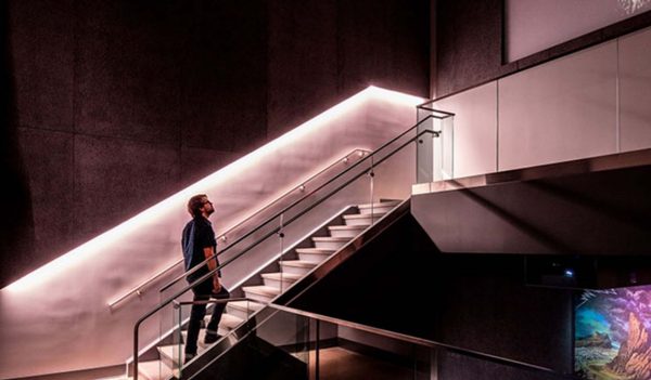 Person walking up stairs to the next level in the museum with lighting along the wall.
